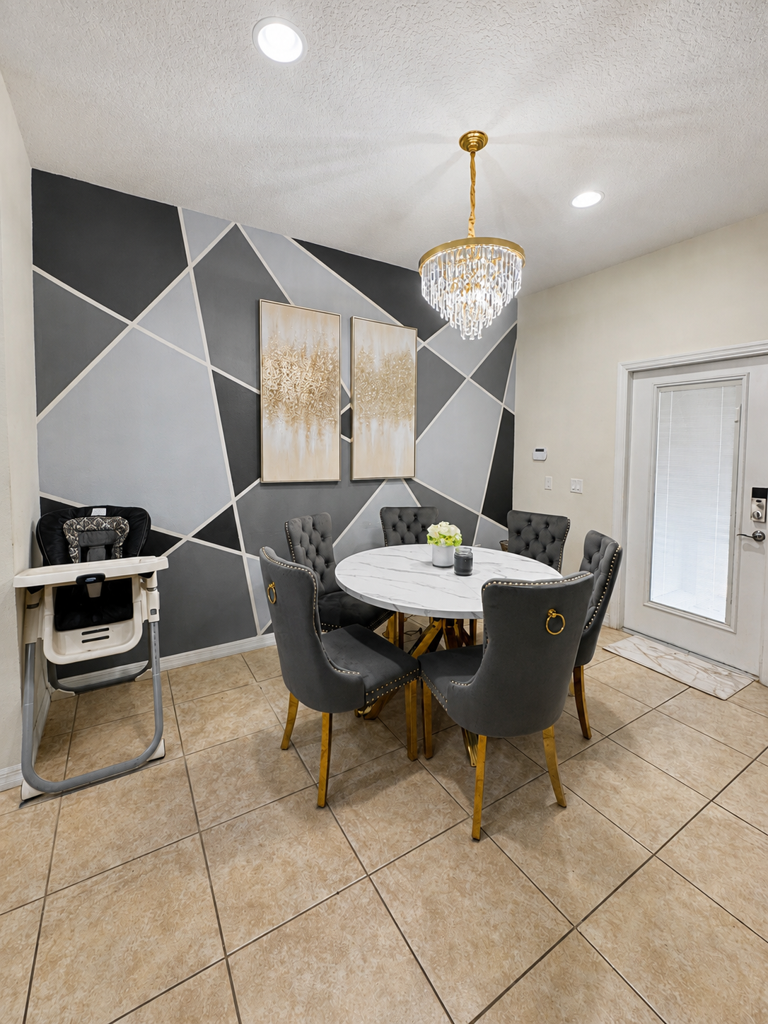 Dining room with geometric accent wall, marble table, and gold chandelier
