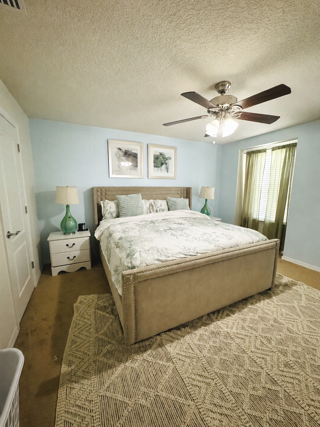 Master bedroom with upholstered king bed, blue accent wall, and ceiling fan